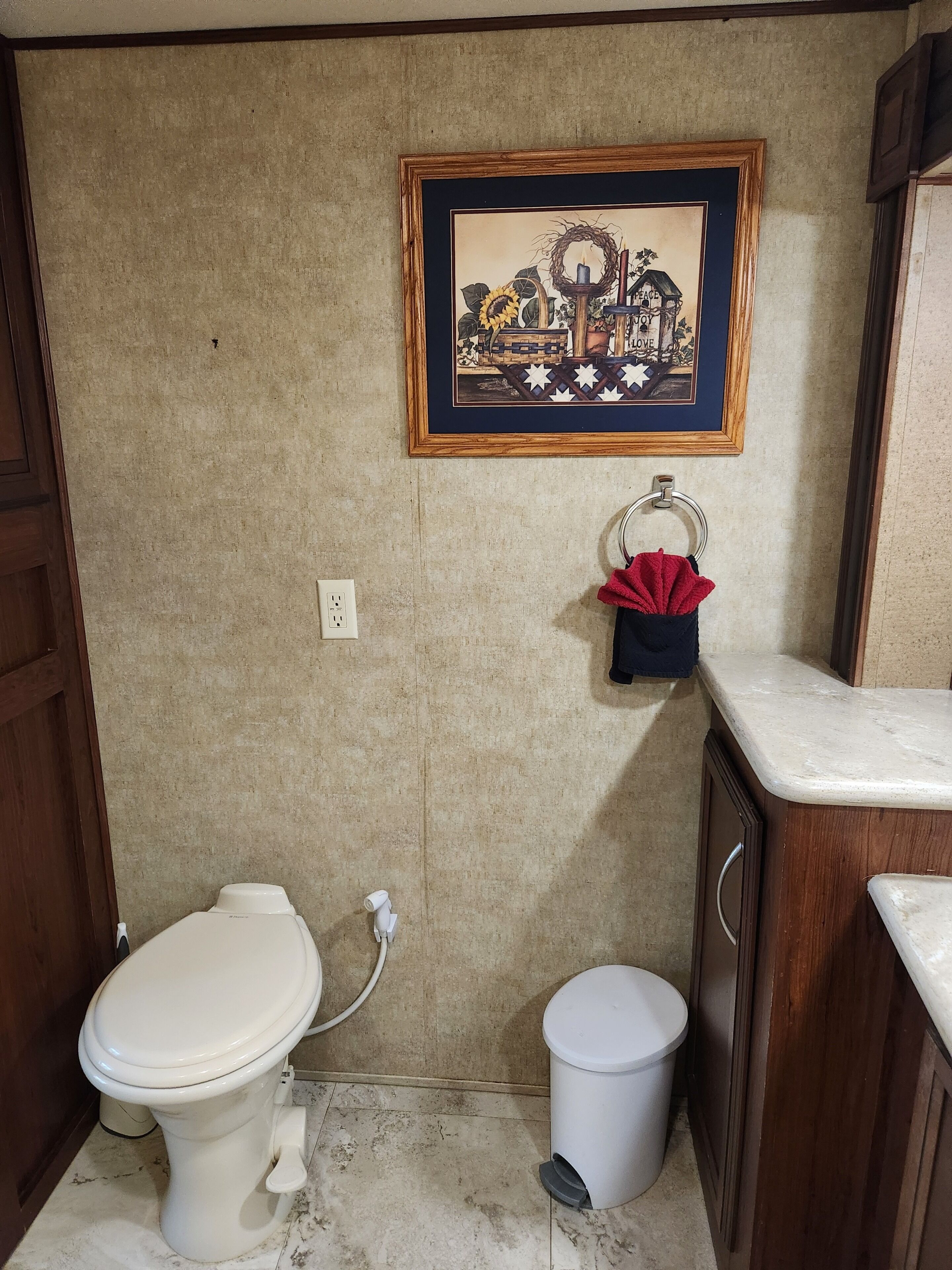 A small bathroom with a toilet, a trash bin, a sink, and a framed picture on the wall.