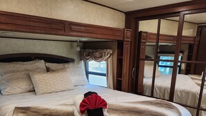 A bedroom with a large bed, a window with curtains, and a view of the outside. - Beautiful 5th wheel with 4 slides in point blank (Point Blank)