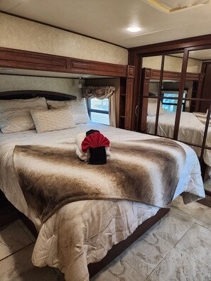 Een slaapkamer met een groot bed, een raam met gordijnen en uitzicht op het omliggende landschap.