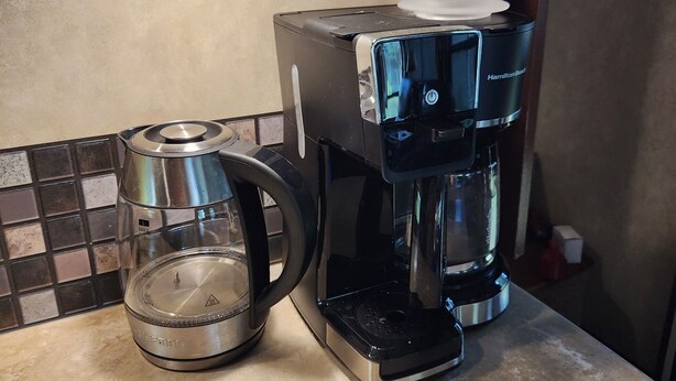 A kitchen with a coffee maker, a glass carafe, and a tiled backsplash.