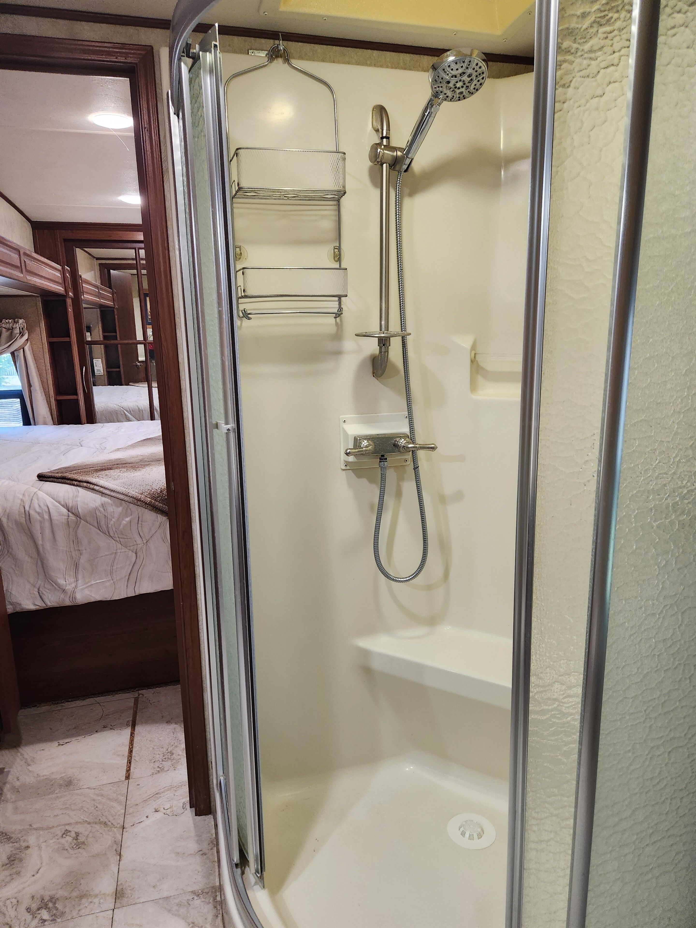 Une douche fermée par des parois en verre, dotée d’un pommeau de douche à main, d’une étagère intégrée et d’un panneau de commande.