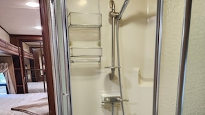 A glass-enclosed shower with a handheld showerhead, a built-in shelf, and a control panel. - Beautiful 5th wheel with 4 slides in point blank (Point Blank)