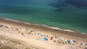 Luchtbeeld van een strand met mensen en kleurrijke parasols.