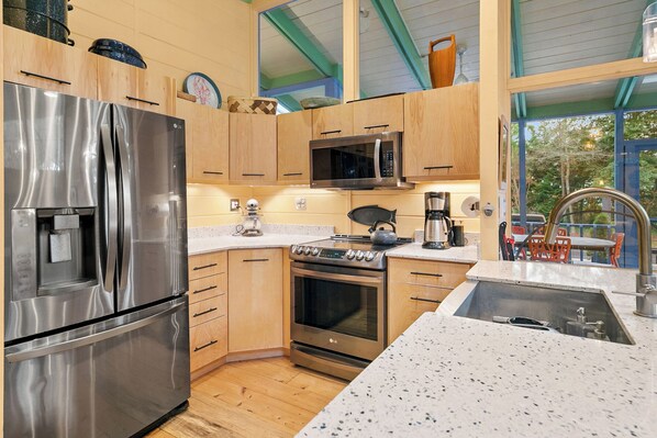 A kitchen with stainless steel appliances, wooden cabinets, a microwave, and a large window.