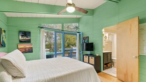 Een slaapkamer met een bed, een plafondventilator, een televisie en een zichtbare badkamer door een geopende deur.