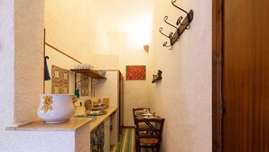 A narrow kitchen with a wooden counter, a white bowl, a small table with cups, a chair, and a red painting on the wall. - Tenuta Donna Vittoria Bouganville Apartment with Mountain View, Wi-Fi & Air Conditioning (Trapani)