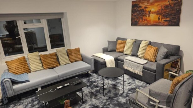 A modern living room with a grey sofa, a coffee table, and a small armchair. A painting hangs on the wall above the sofa. - Stylish Stay in Brighton: London Road Gem (Brighton and Hove)