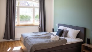 A bedroom with a bed, a window with curtains, a radiator, and a bedside table. - BEST STAY Rhönzauber Dietershausen (Künzell)
