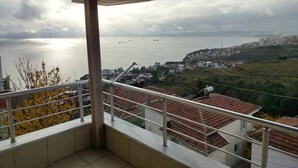 A balcony with a view of a coastal town, a body of water, and ships in the distance. - Quiet and Comfortable in Sinop Karakum Site 2 (Sinop)