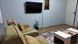 A living room with a sofa, a television mounted on the wall, a small plant, and a patterned rug. - Quiet and Comfortable in Sinop Karakum Site 2 (Sinop)
