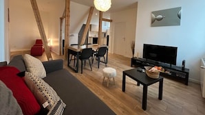 Una sala de estar moderna con sofá, mesa de comedor, sillas, televisor y piso de madera.
