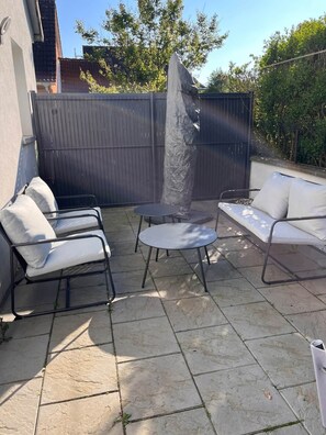Une terrasse avec une table ronde, deux chaises blanches dotées de coussins, un canapé et une grande sculpture en pierre.