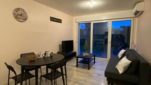 Ett vardagsrum med ett matbord, stolar, en soffa, en TV och en skjutdörr i glas som leder ut till ett utomhusområde.