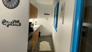 Un couloir avec une horloge, une affiche sur laquelle on peut lire « Carpe Diem », un petit tapis et une fenêtre avec des bordures bleues.