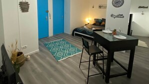 Une pièce de taille modeste comprenant un lit, une table à manger avec des chaises, un petit tapis et une horloge murale.
