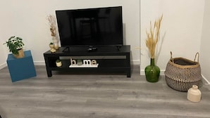 Un meuble de rangement noir pour appareils électroniques, avec un téléviseur, un élément décoratif bleu, une petite plante en pot, un vase contenant des plantes séchées et un panier tressé.