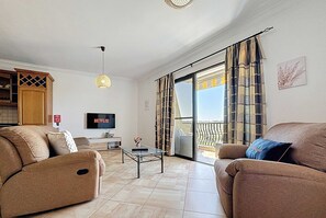 A living room with a sofa, a coffee table, a TV, and a balcony with curtains. - Seaside Retreat with Balcony Views in Marsaskala (Wied il-Għajn)