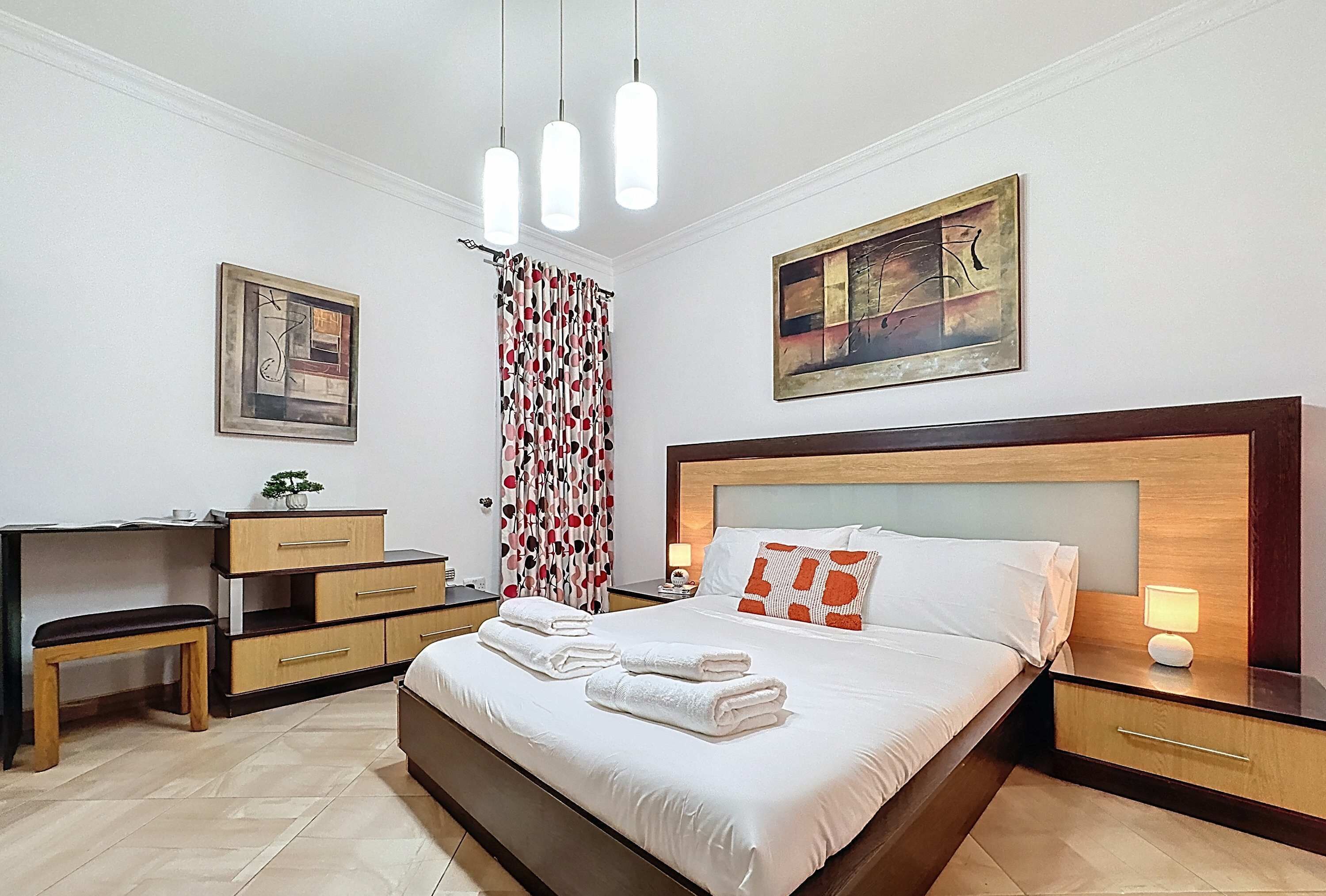 Un cuarto de hotel ordenado, con una cama, mesitas de noche, un escritorio y un banco.