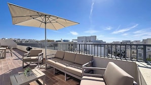 A rooftop terrace with a sofa, chairs, a table, and an umbrella. - Mosta Couples Retreat - Sunny Rooftop 2BR (Il-Mosta)