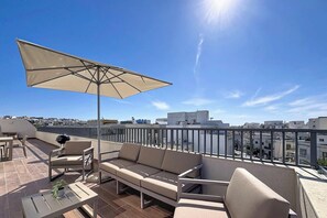 Eine Dachterrasse mit einer Couch, Stühlen, einem Tisch und einem Sonnenschirm.