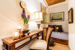 A bedroom with a bed, a bedside table with a lamp, a chair, a desk with a lamp, and a wall-mounted mirror. - Epidavros Villas - Gardenia Garden Retreat w Pool (Epidaurus)
