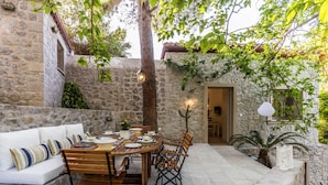 A stone-walled outdoor dining area with a wooden table and chairs, a white sofa, and a potted plant. - Epidavros Villas - Rodia Garden Retreat (Epidaurus)