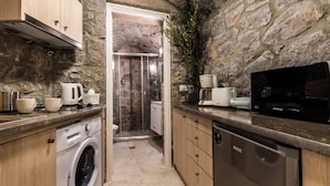 A compact kitchen with a stone wall, a washing machine, a dishwasher, and a microwave. - Epidavros Villas - Rodia Garden Retreat (Epidaurus)