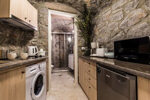 A compact kitchen with a stone wall, a washing machine, a dishwasher, and a microwave. - Epidavros Villas - Rodia Garden Retreat (Epidaurus)