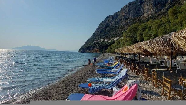A beach with sun loungers and umbrellas, a rocky cliff, and a clear view of the sea. - Epidavros Villas - Rodia Garden Retreat (Epidaurus)