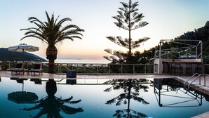 A swimming pool with lounge chairs and umbrellas, a stone building, and a view of hills and a sunset. - Epidavros Villas - Elia Garden Retreat w Pool (Epidaurus)