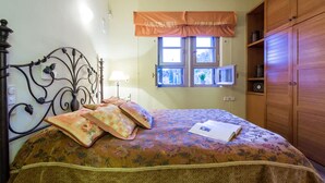 A bedroom with a bed, a window with curtains, a bedside table, and a wardrobe. - Epidavros Villas - Elia Garden Retreat w Pool (Epidaurus)