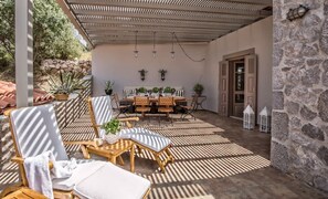 An outdoor patio with a table set for dining, surrounded by chairs, and a covered seating area with sunshades. - Epidavros Villas Thymari Garden Seaview Retreat (Epidaurus)