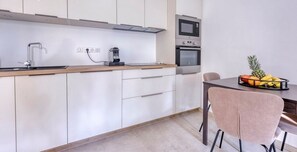 Eine moderne Küche mit weißen Schränken, einer Edelstahl-Spüle, einer Mikrowelle und einem Backofen. Es gibt eine Holz Arbeitsplatte und ein Stuhl mit einer Obstschale auf dem Tisch.