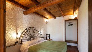 Un dormitorio con una cama, techo de madera, pared texturizada y lámpara fijada a la pared.