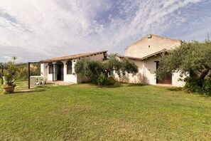 Ein Haus mit Garten, einer Terrasse mit Stühlen und einer überdachten Außenbereich-Sitzgelegenheit.