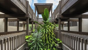 A corridor with wooden railings and a central plant. - Kona Mansions#B217 2nd Floor, Beautiful unit/Ocean views & Air Conditioning (Kailua Kona)