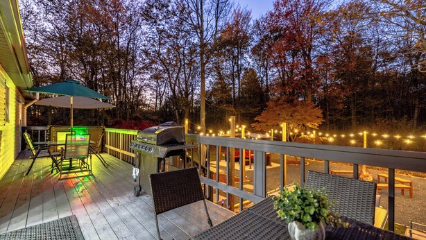 Una terraza de madera con mobiliario exterior, una parrilla y luces colgantes.