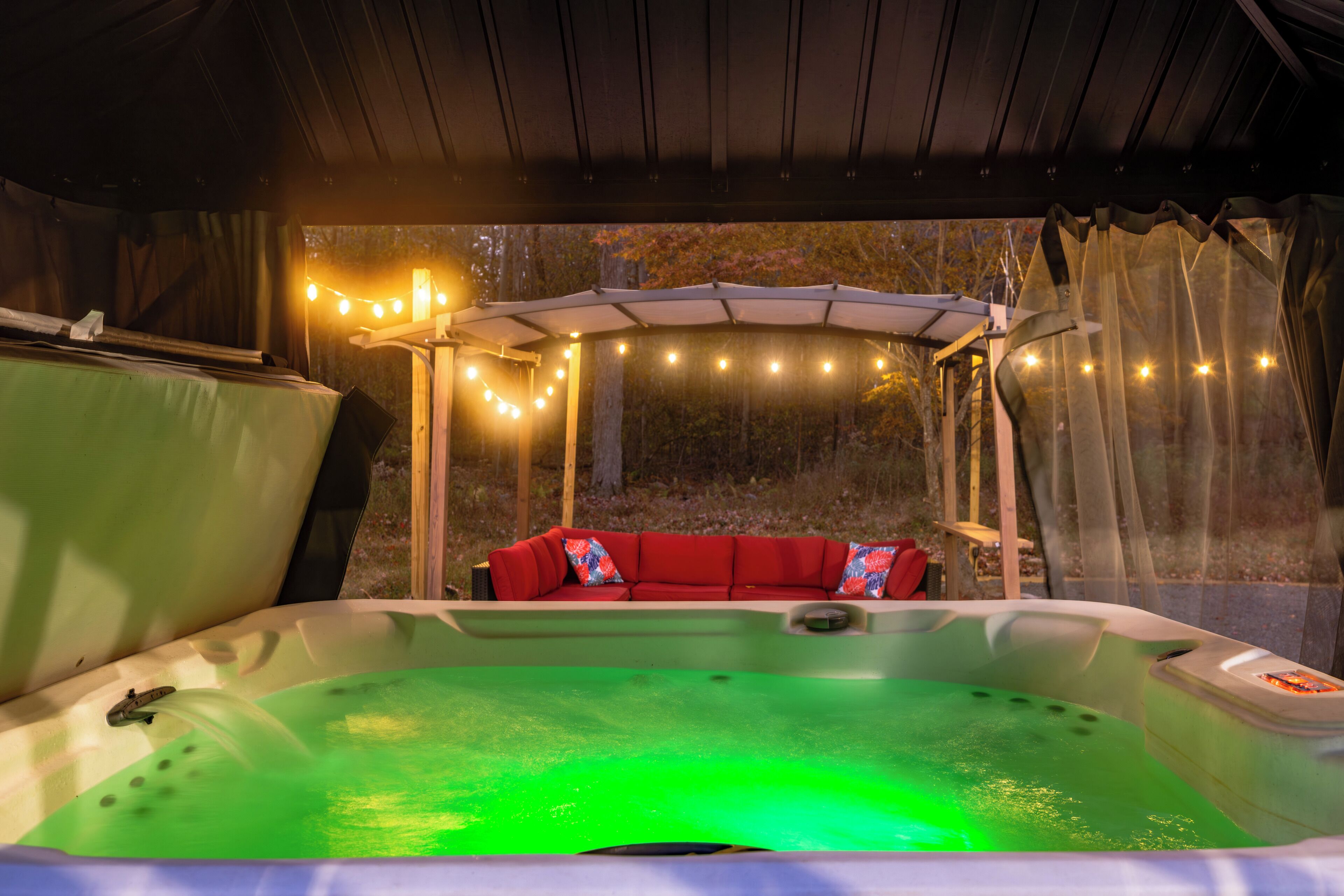 A hot tub with a green light, a red couch, and string lights.