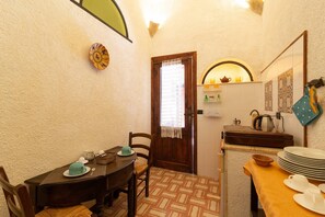 A compact kitchen with a dining table, chairs, a small refrigerator, and a window with a curtain.