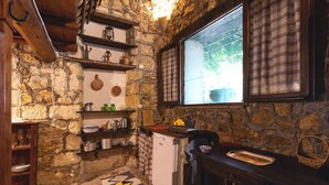 A rustic kitchen with stone walls, wooden shelves, a small refrigerator, and a window with plaid curtains. - Apartment 'Tenuta Donna Vittoria Piccola' with Mountain View, Wi-Fi and Air Conditioning (Trapani)