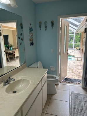 Ein Badezimmer mit Waschbecken, Toilette und einer Tür zum Poolbereich.