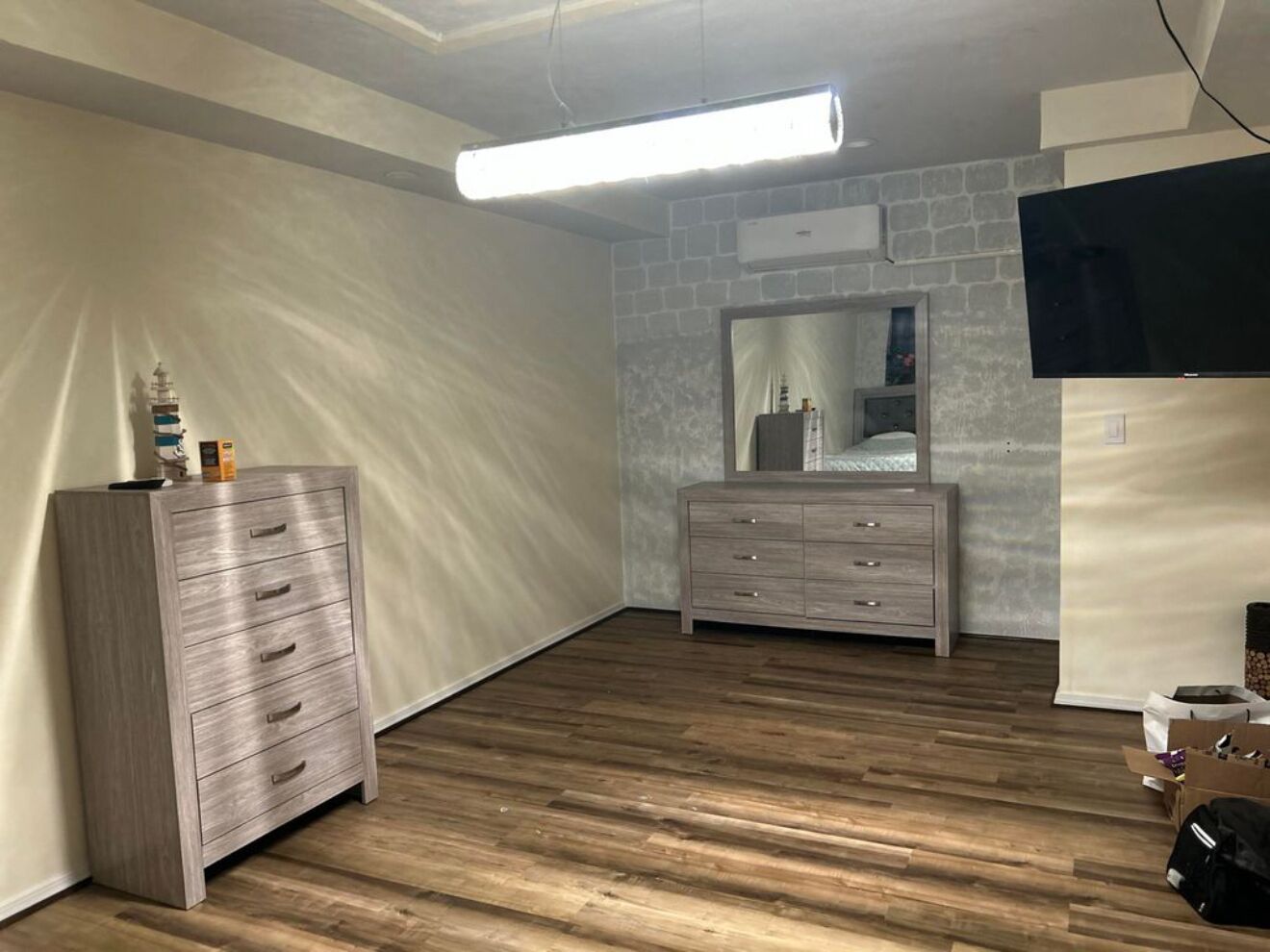Une pièce avec un plancher en bois, deux commodes, un miroir et un téléviseur à écran plat.