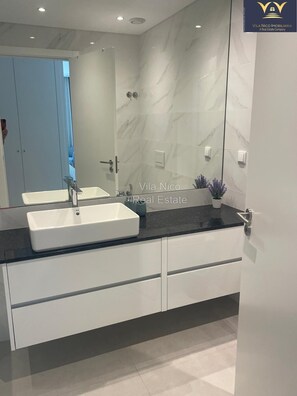 A modern bathroom with a large mirror, white cabinetry, and a marble backsplash. - Beautiful 2 bedroom/2 bath Luxury Apartment with Pool and Sea view (Lagos)