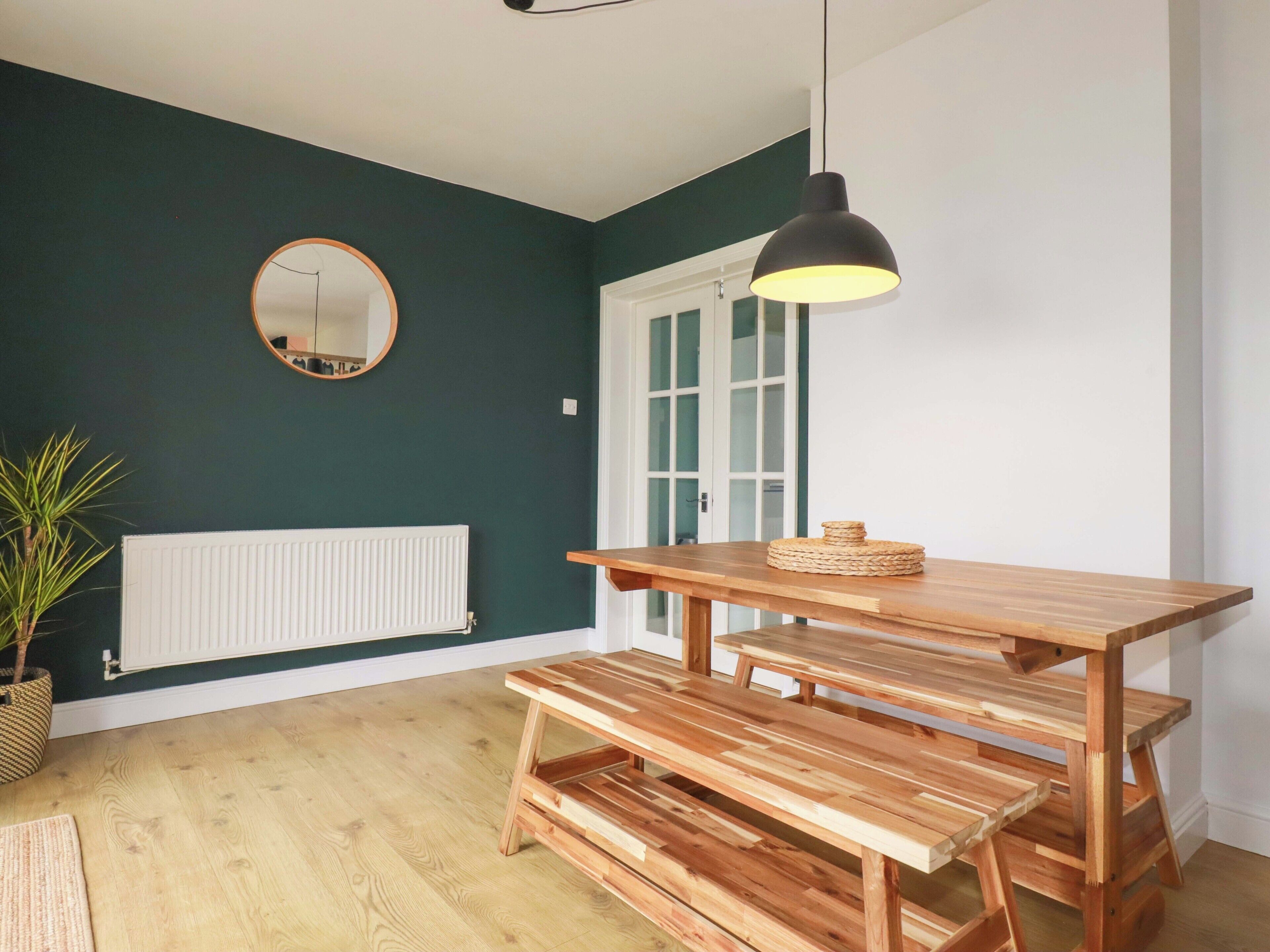 Una habitación con un banco de madera, una lámpara colgante, un espejo redondo y un radiador.