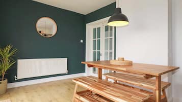 Una habitación con un banco de madera, una lámpara colgante, un espejo redondo y un radiador.
