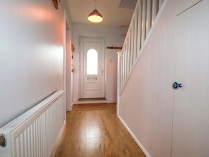 A hallway with a white door, wooden flooring, a radiator, and a ceiling light fixture. - Trelowen (Wadebridge)