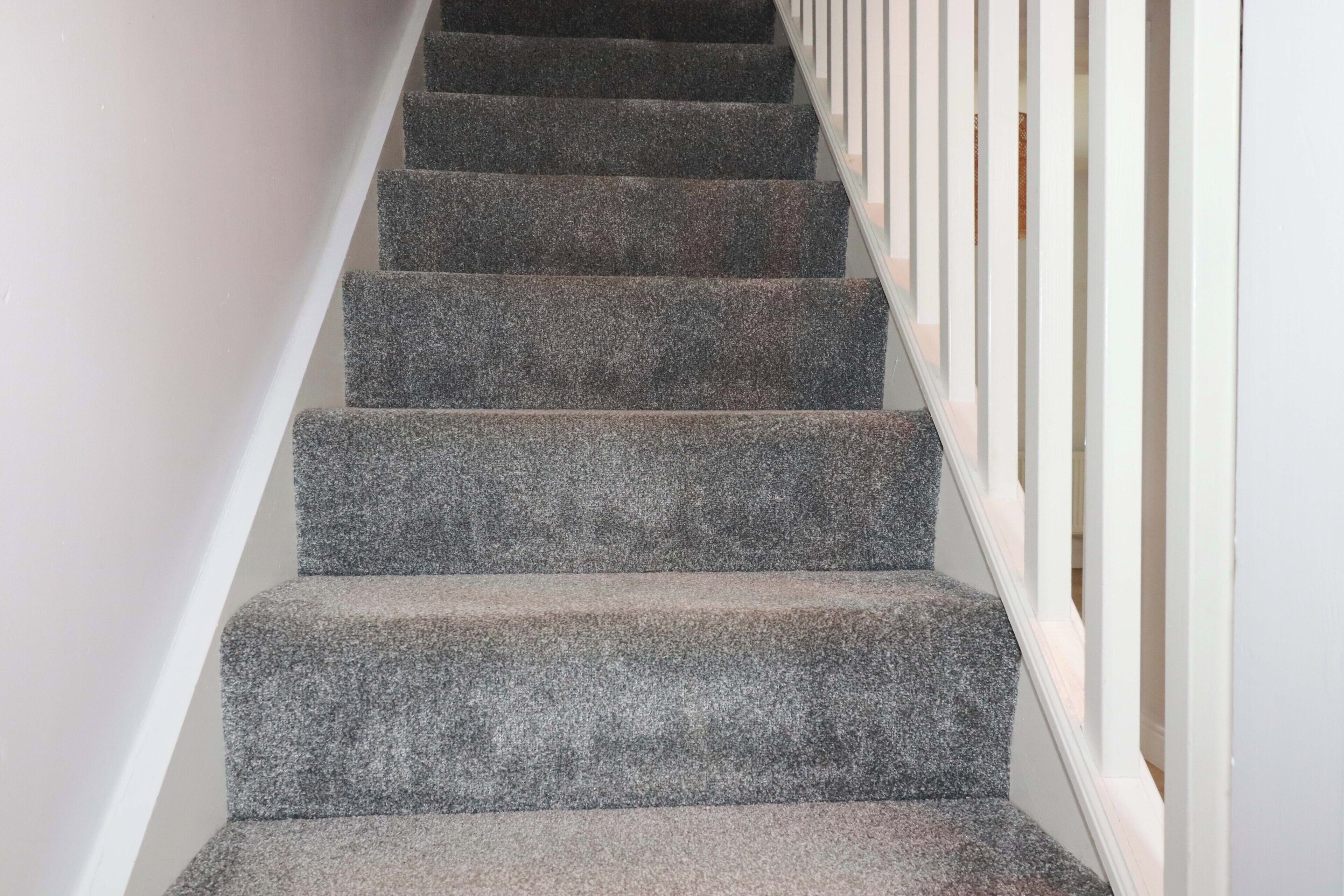 Una escalera con peldaños alfombrados y barandillas blancas.