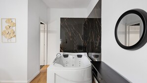 Ein modernes Badezimmer mit einer weißen Badewanne, einem großen Spiegel und einer Marmor-Spritzschutzwand.