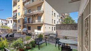 Ein Balkon mit Tisch und Stühlen, Blumentöpfen und Blick auf eine Straße mit abgestellten Rollern.