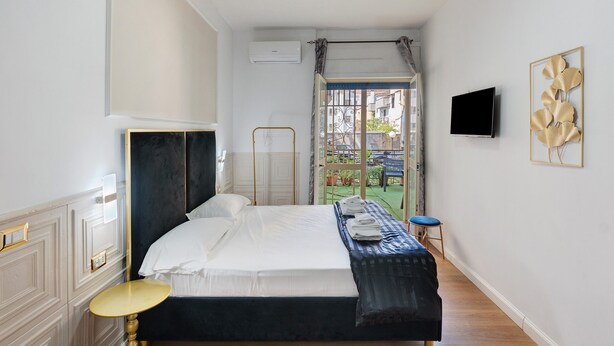 Ein Schlafzimmer mit Bett, Fernseher, einem Fenster mit Vorhängen und Blick ins Freie.